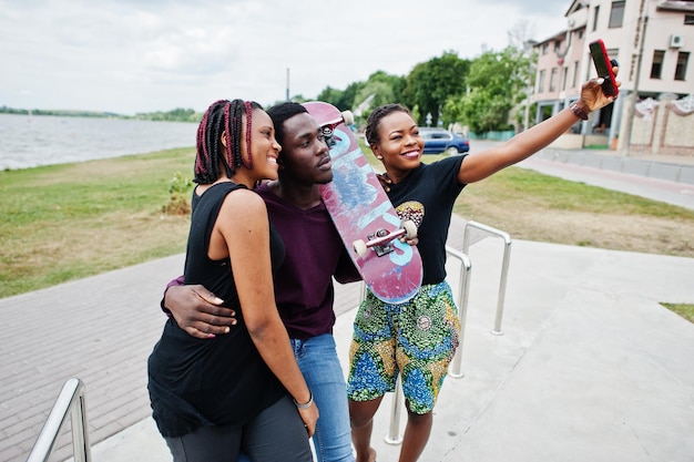 Grupa trzech afroamerykańskich przyjaciół z deskorolką robi selfie na telefonie