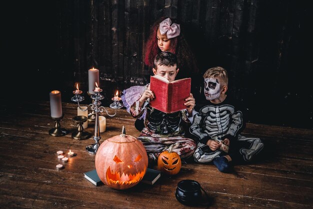 Grupa uroczych wielorasowych dzieciaków w przerażających kostiumach czytających horrory w starym domu podczas imprezy Halloween. Koncepcja Halloween.