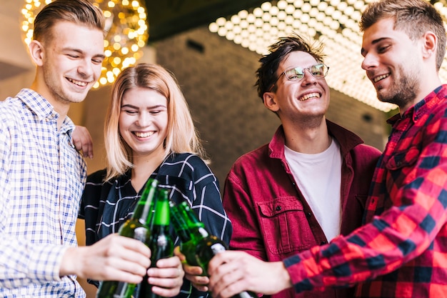 Bezpłatne zdjęcie grupa uśmiechnięci przyjaciele wznosi toast piwo butelki w pubie