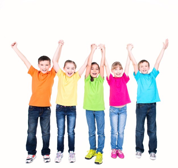 Grupa uśmiechniętych dzieci z uniesionymi rękami w kolorowe t-shirty stojące razem - na białym tle.