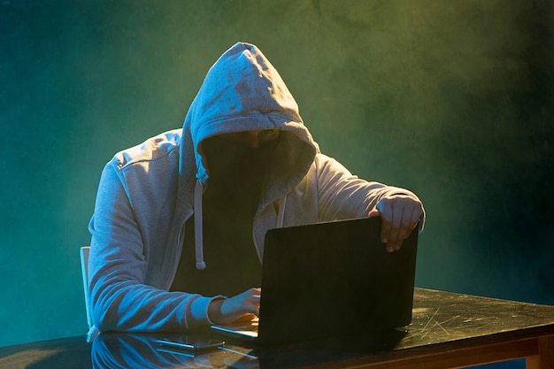 Haker z kapturem kradnie informacje za pomocą laptopa
