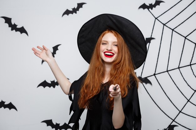 Halloween Concept - piękna czarownica bawi się magicznym kijem na szarej ścianie.