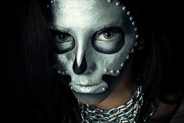 Halloween, święta, styl życia, ludzie, piękno, kreatywna koncepcja - halloween i kreatywny makijaż temat: piękna dziewczyna model z czarnym ciałem ze srebrną farbą czaszki maski na ciemnym tle w studio