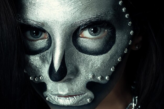 Halloween, święta, styl życia, ludzie, piękno, kreatywna koncepcja - halloween i kreatywny makijaż temat: piękna modelka z czarnym ciałem ze srebrną farbą czaszki maski na ciemnym tle w studio
