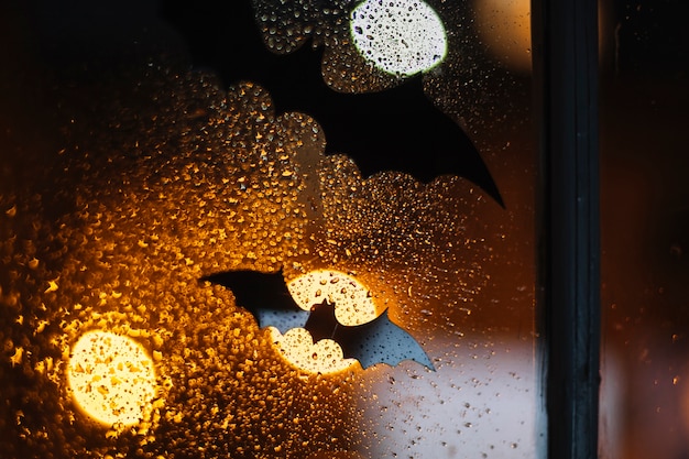 Halloweenowi czarni dekoracyjni nietoperze zablokowani na okno z raindrops