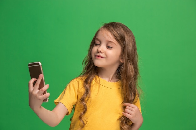 Happy teen girl stojącej, uśmiechając się z telefonu komórkowego nad modną zieloną ścianą studio