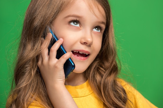 Happy Teen Girl Stojącej, Uśmiechając Się Z Telefonu Komórkowego W Modnym Zielonym Studio.