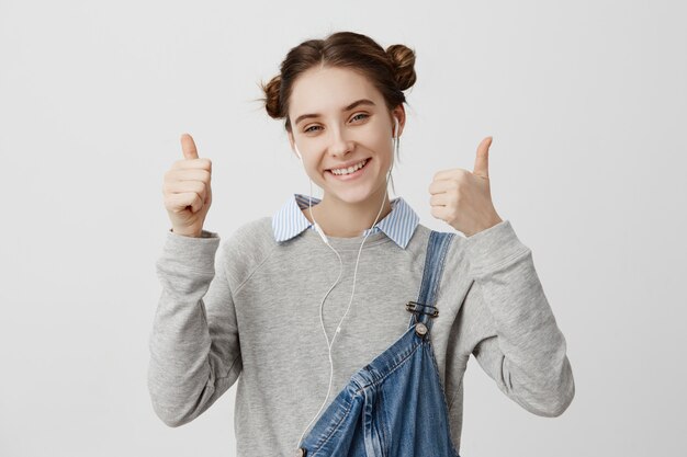 Headshot atrakcyjna kobieta ubrana w dorywczo pozytywnie pozowanie z kciuki do góry. Sympatyczna modelka reklamująca nowe słuchawki w sklepie gestykuluje jak znak.
