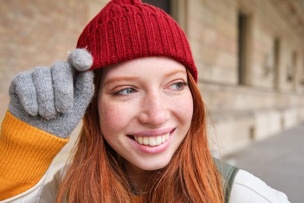 Headshot szczęśliwej rudej dziewczyny z piegami nosi czerwony kapelusz i rękawiczki zimą spaceruje po mieście