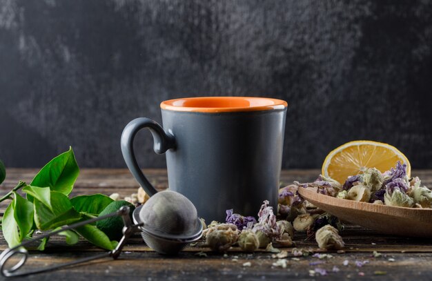Herbata w filiżance z limonkami, sitkiem, ziołami, cytryną, limonkowym widokiem z boku na ciemnej i drewnianej powierzchni