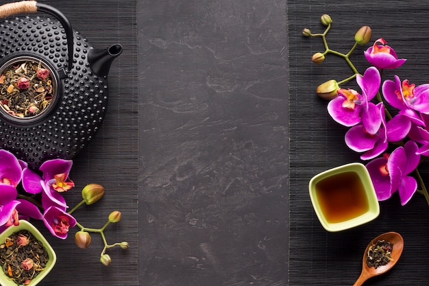 Herbata ziołowa z suszonym składnikiem i kwiatem orchidei na czarnej podkładce
