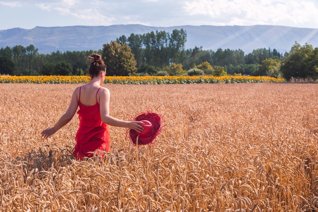 Hipnotyzujące ujęcie atrakcyjnej kobiety w czerwonej sukience pozującej na polu pszenicy