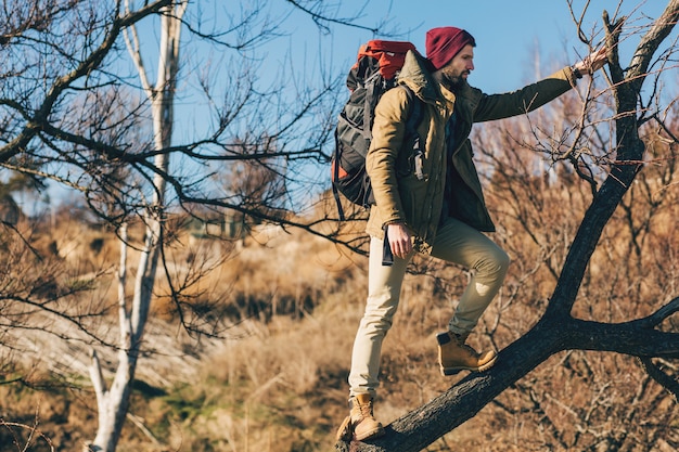 Hipster człowiek podróżujący z plecakiem w jesiennym lesie w ciepłej kurtce, kapeluszu, aktywny turysta, odkrywanie przyrody w zimnych porach roku