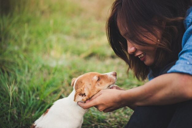 Hipster uśmiech cieszyć się gry z jej puppy w polu latem, rocznik filtra tonu.