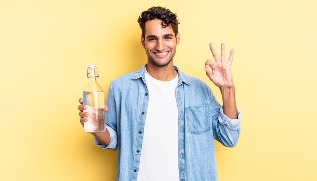 Hiszpanie przystojny mężczyzna czuje się szczęśliwy, okazując aprobatę w porządku gestem. koncepcja butelki z wodą