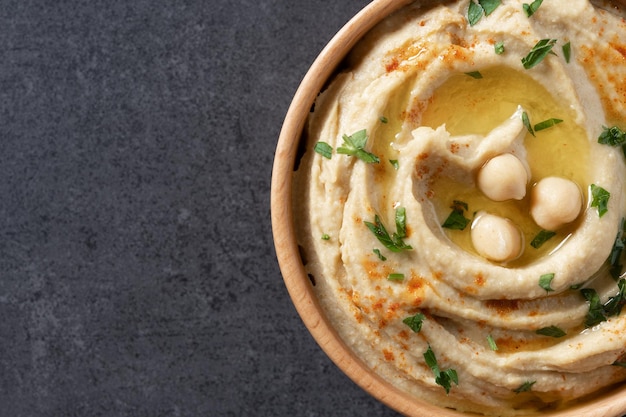 Hummus z ciecierzycy w drewnianej misce przyozdobionej pietruszką, papryką i oliwą z oliwek Z bliska