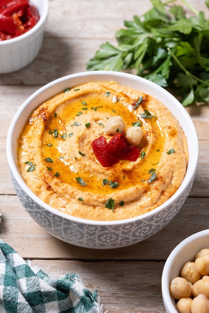 Hummus z pieczonej czerwonej papryki w białej misce na drewnianym stole