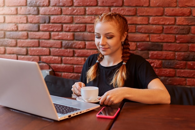 Imbirowa dziewczyna używa laptopa w kawiarni