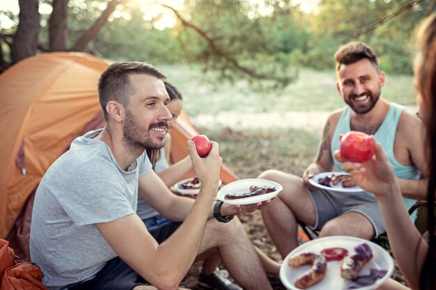 Impreza, biwakowanie grupy mężczyzn i kobiet w lesie. relaks i jedzenie grilla na zielonej trawie. wakacje, lato, przygoda, styl życia, koncepcja pikniku