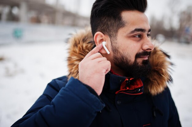 Indianin z brodą nosi kurtkę w zimny zimowy dzień Słuchawki mobilne w uszach