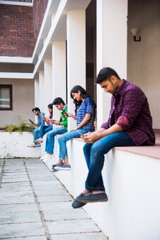 Indyjska azjatycka grupa studentów używających smartfonów do mediów społecznościowych, wysyłania sms-ów, oglądania filmów