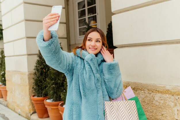 Inspirowana brązowowłosa dziewczyna robi selfie po robić zakupy i śmia się.