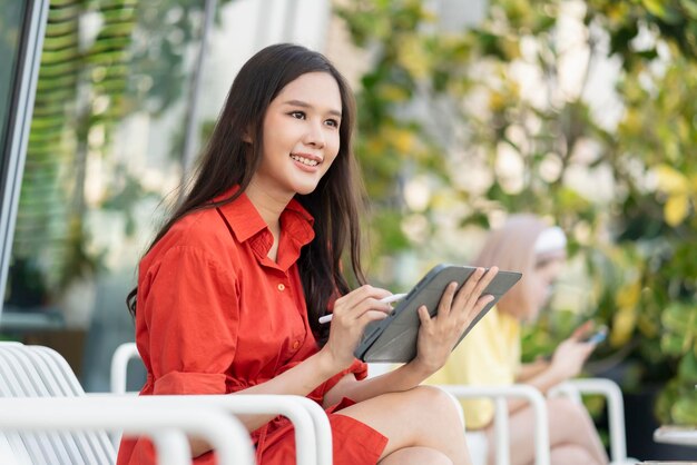 Inteligentna atrakcyjna azjatycka kobieta dorywczo tkaniny freelance praca wypoczynek relaks praca z tabletem i smartfonem w kawiarni restauracja miejski styl życia cyfrowy nomada pracująca w przestrzeni roboczej