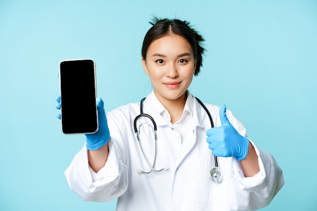 Internetowa opieka zdrowotna online koncepcja pomocy pewna azjatycka lekarka lub pielęgniarka pokazująca ekran smartfona ...