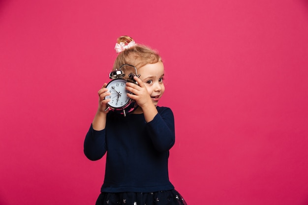 Bezpłatne zdjęcie intrygująca młoda blondynki dziewczyna trzyma budzika nad menchii ścianą