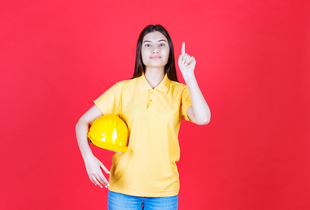 Inżynier dziewczyna w żółtym dresscode trzymająca żółty hełm ochronny i pokazująca gdzieś