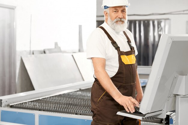 Inżynier w kasku pracy z wycinarką laserową, pozowanie.