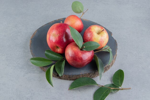Jabłka i liście zawinięte na drewnianej desce na marmurze.