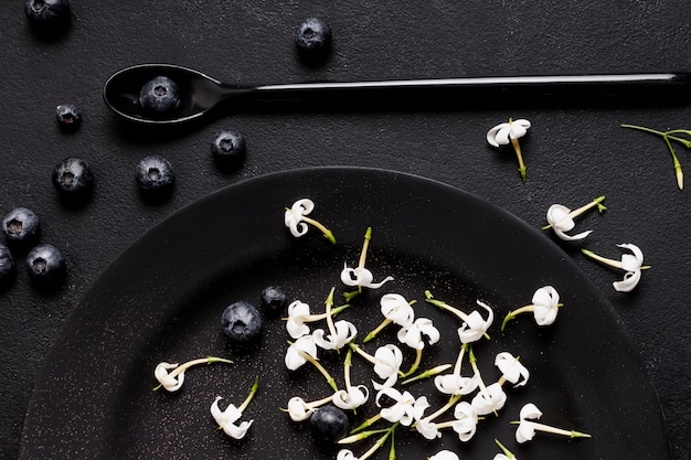 Bezpłatne zdjęcie jagody płasko leżały na ciemnym talerzu z kwiatami