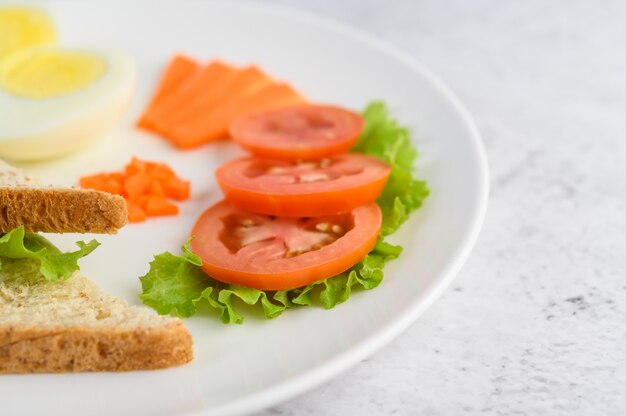 Jajka na twardo, chleb, marchewki i pomidory na białym talerzu z nożem i widelcem.