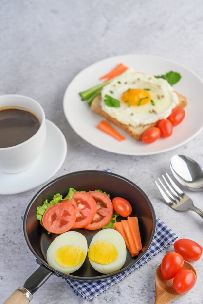 Jajka na twardo, marchewki i pomidory na patelni z pomidorami na drewnianej łyżce i filiżance kawy.