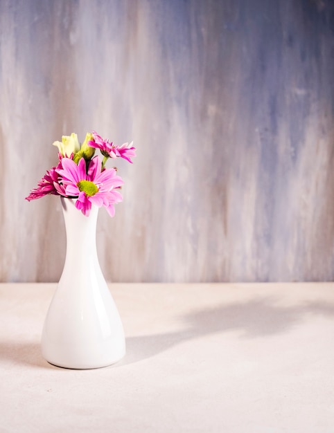 Jaskrawi kwiaty w białym wazie na stole