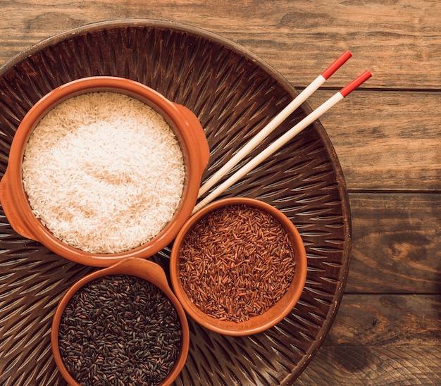Jaśminowy czerwony ryż; czarny ryż i biały ryż na drewnianej tacy z pałeczkami
