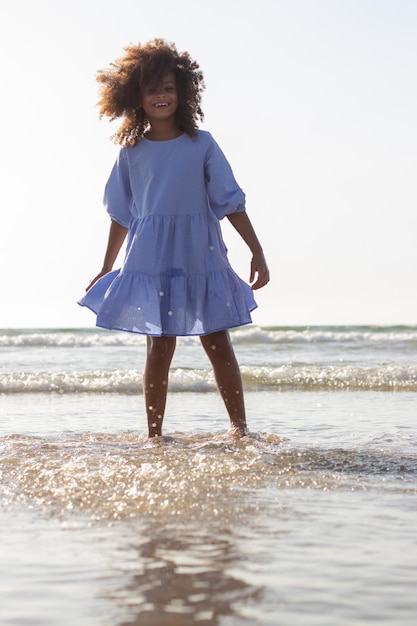 Jasna dziewczynka w sukience na plaży. African American dziecko na plaży w letni dzień, zalewaniem, uśmiechając się. Dzieciństwo, wakacje, koncepcja szczęścia