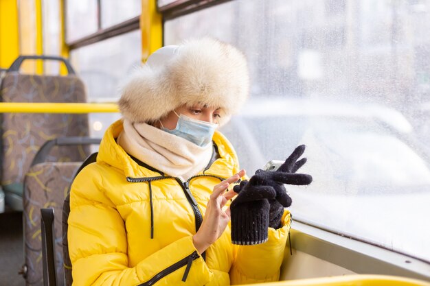 Jasny słoneczny portret młodej kobiety w ciepłych ubraniach w autobusie miejskim w zimowy dzień z telefonem komórkowym w dłoni