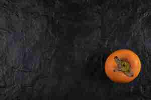 Bezpłatne zdjęcie jeden dojrzały owoc persimmon umieszczony na czarnej powierzchni