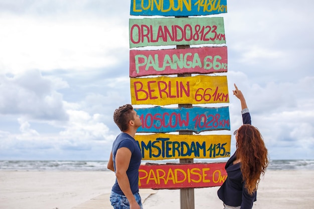 Bezpłatne zdjęcie jeden facet i ruda dziewczyna pozowanie na drogowskaz na plaży.