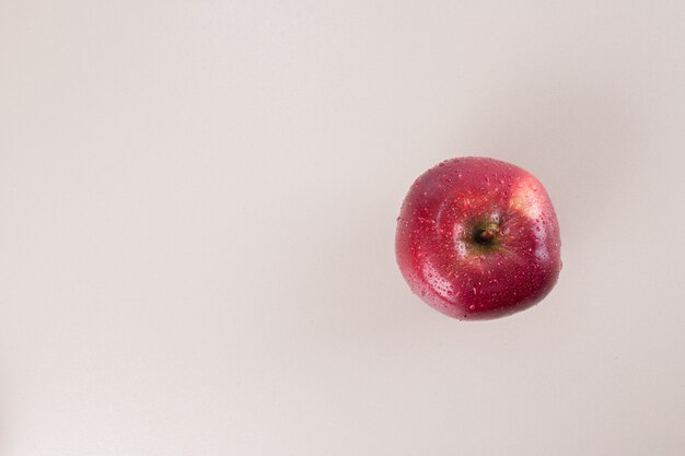 Jedno czerwone jabłko na białej powierzchni.