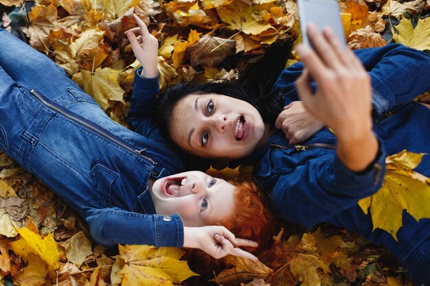 Jesienne wibracje, portret rodzinny. Urocza mama i jej córeczka z rudymi włosami bawią się, biorąc selfie na sm