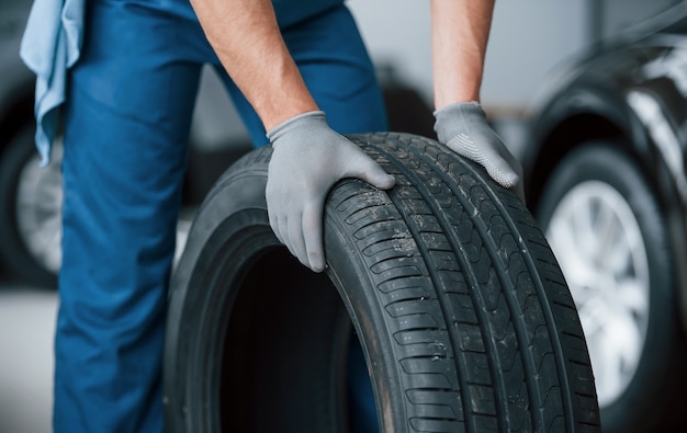 Bezpłatne zdjęcie jeszcze jedno ulepszenie i praca zostanie wykonana. mechanik trzymający oponę w warsztacie naprawczym. wymiana opon zimowych i letnich