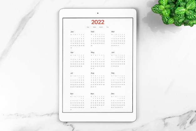 Kalendarz 2022. komputer typu tablet z otwartą aplikacją. białe tło marmuru, pulpit biznesowy, do celów i planowania koncepcji nowego roku. widok z góry, płasko leżące zdjęcie