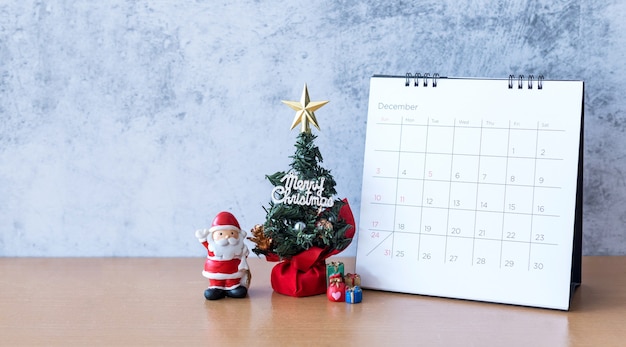 Kalendarz grudnia i świąteczne dekoracje - mikołaj, drzewo i prezent na drewnianym stole. koncepcja bożego narodzenia i szczęśliwego nowego roku