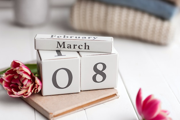 Kalendarz z datą 8 marca, książka i kwiat na białym stole