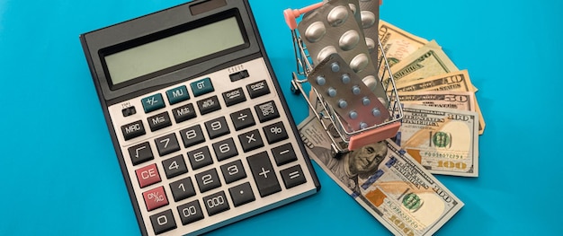 Kalkulator z nowymi dolarami na koszyku, w którym tabletki leżą na niebieskim tle. koncepcja zakupów.