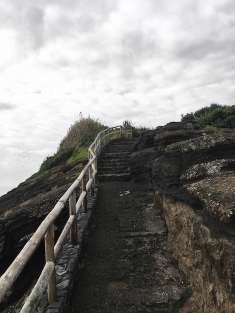 Kamienne schody w kierunku szczytu wzgórza z drewnianą poręczą pod pochmurnym szarym niebem po deszczu