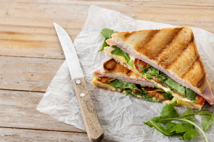 Bezpłatny plik Zdjęcie kanapka panini z szynką, serem, pomidorem i rukolą na drewnianym stole
